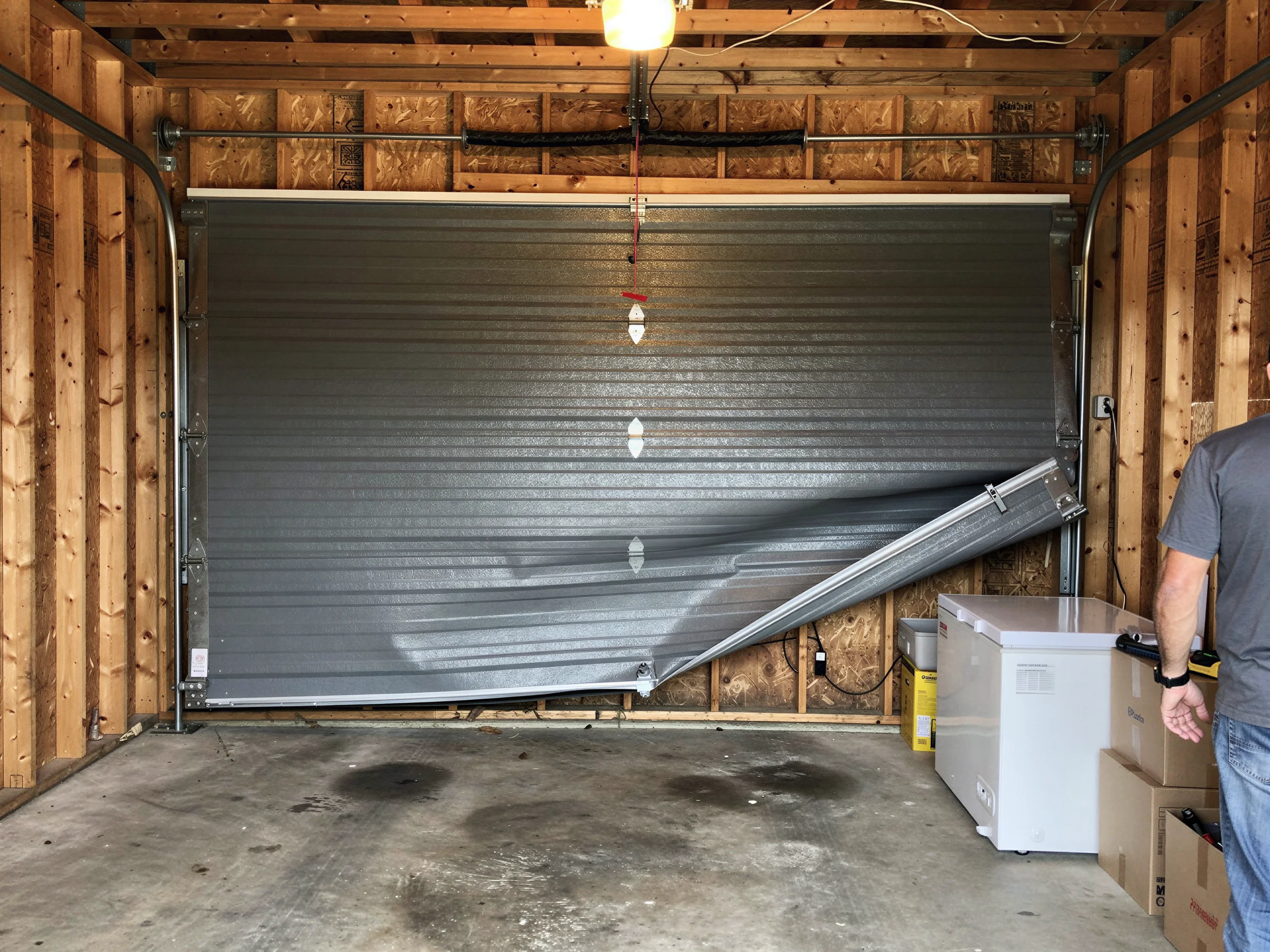 The gray garage door is bent and partially detached from its tracks.